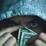 a man with a hoodie with eyes glaring and dollar bills in his hands