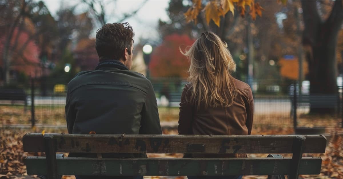 the back of a woman and man sitting on a bench with trees in background