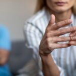 female taking off wedding ring, male in background, concept of Divorce vs. Dissolution of Marriage