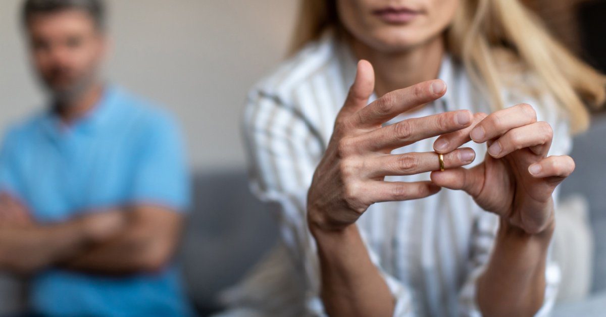 female taking off wedding ring, male in background, concept of Divorce vs. Dissolution of Marriage